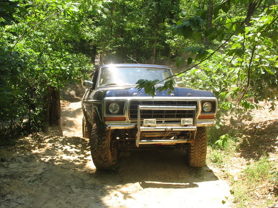 Front view of a 1978 Ford Bronco driving on a dirt trail through trees