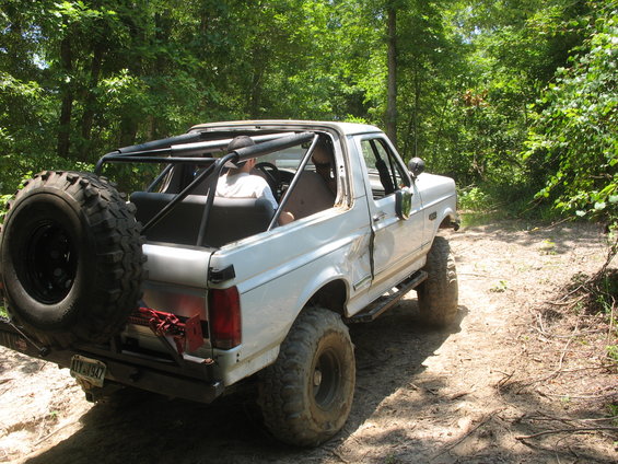 White SUV with roll cage, spare tire, and off-road tires on a dirt path