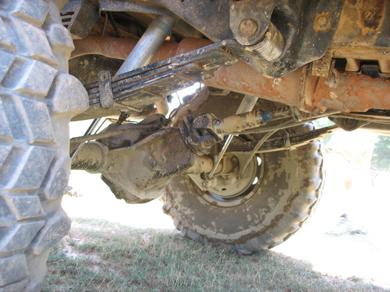 Underside of a vehicle showing leaf springs, driveshaft, and large tires