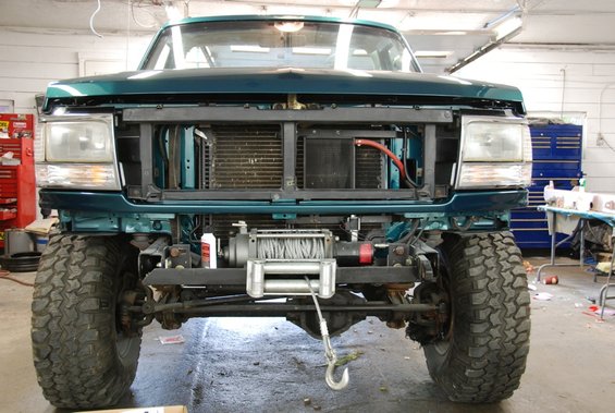 Front view of a teal Ford F-Series truck with its grille removed, showing the radiator and a winch mounted on the bumper