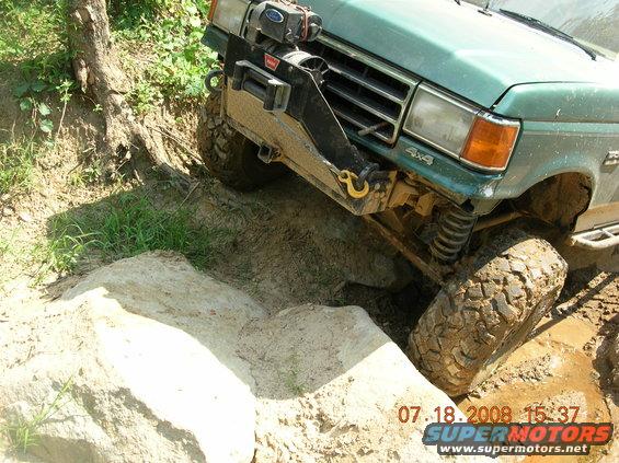 Green 1991 Ford F-150 with winch and aftermarket bumper navigating rocky terrain
