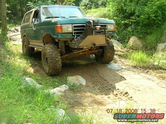 Green 1991 Ford Bronco off-roading on a muddy trail