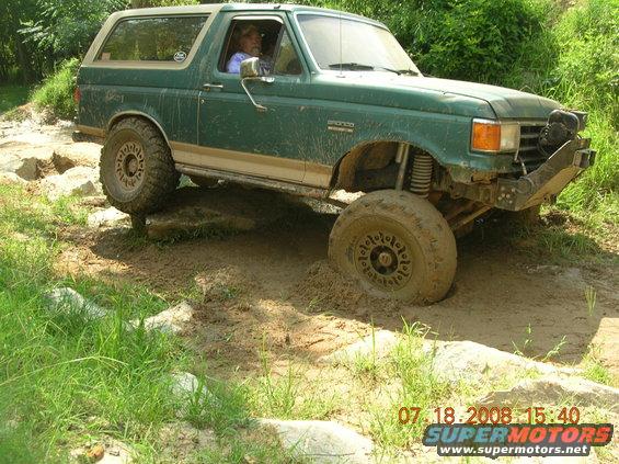 Green Ford Bronco with lifted suspension and off-road tires navigating a muddy trail