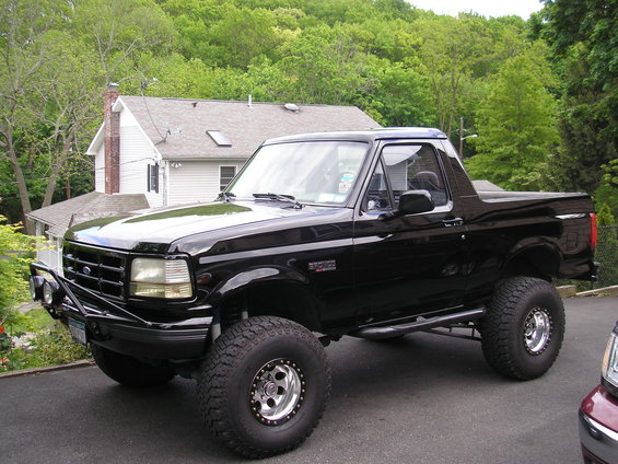 Black Ford Bronco with aftermarket bumper and large tires, parked on asphalt