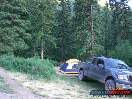 Dark blue Ford F-150 parked next to a tent at a campsite in a forest