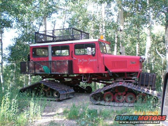 Red tracked vehicle with 'San Juan Snocats' on the side, parked in a wooded area
