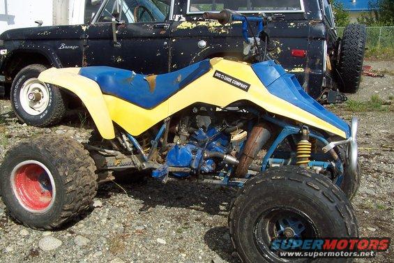 Yellow and blue ATV parked in front of a black Ford Bronco. Text on ATV reads 'DVS O SHOE COMPANY'