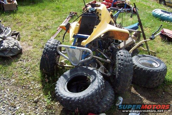 Yellow and blue all-terrain vehicle with flat tires and a bent metal bumper, resting on grass