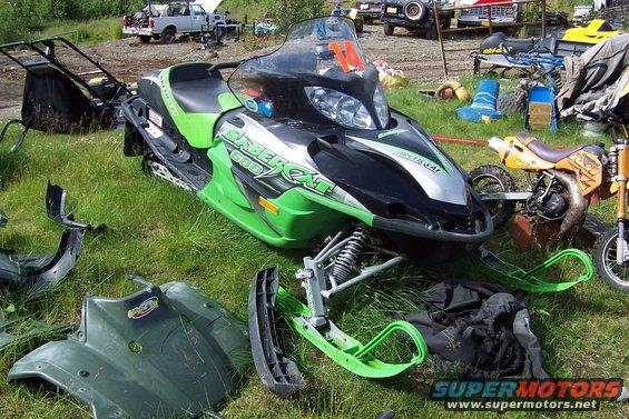 Green and black Arctic Cat snowmobile with "Saber Cat 600" visible, parked on grass with parts scattered around