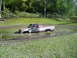 1995 Mercury Grand Marquis - A red and white pickup truck is stuck in a muddy puddle with trees in the background.