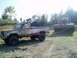 1995 Mercury Grand Marquis - A lifted pickup truck tows a large excavator bucket across a muddy field under a bright sky.