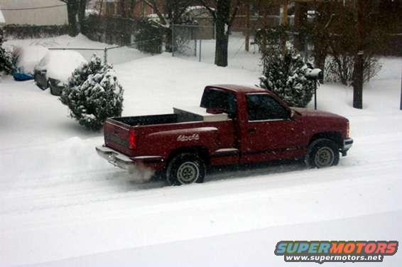 Red pickup truck driving in snow, 3q-front view