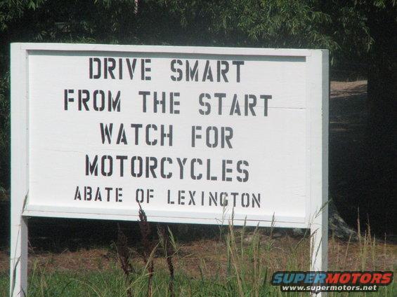 White sign with black text reading "DRIVE SMART FROM THE START WATCH FOR MOTORCYCLES ABATE OF LEXINGTON"