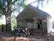 2006 Victory Kingpin - A black motorcycle sits parked beside an old, weathered wooden shed under a large tree. A sign on the tree indicates 'BOOTH 1'.