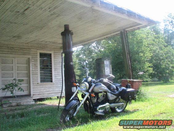 Motorcycle parked by an old gas pump next to a weathered building