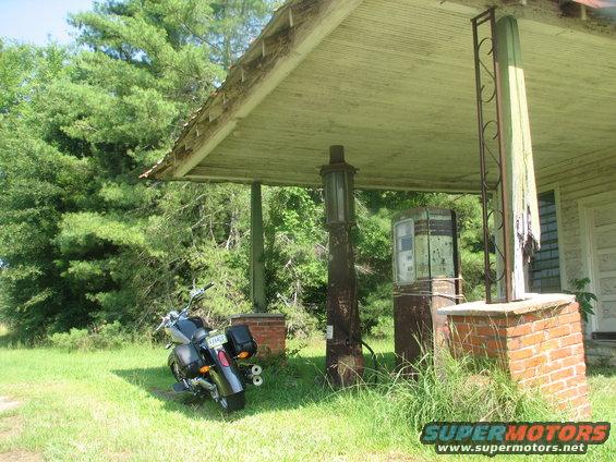 Motorcycle parked at abandoned gas station with vintage pumps
