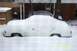 1991 Ford Crown Victoria LTD - A white sedan is almost completely covered by a thick layer of snow, with another vehicle partially visible behind it.