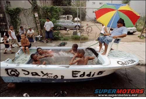 Kids and adults in a boat filled with water, with names 'Jayson' and 'Eddie' painted on the side. A man sits under an umbrella