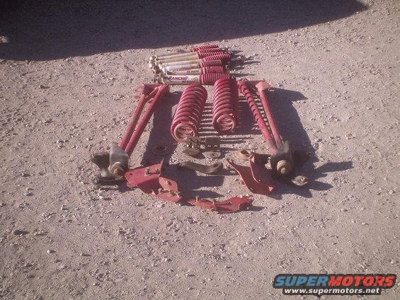 Several red suspension components and Rancho shocks laid out on gravel