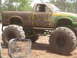 1989 Ford Bronco - A heavily muddied pickup truck with massive tires sits off-road, its green paint partially visible.