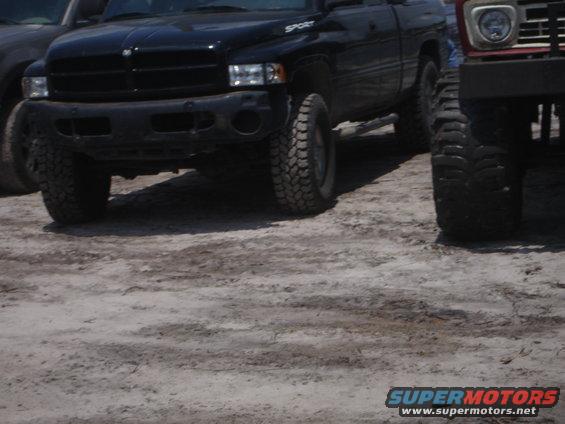 Front view of black pickup truck with lifted tires, next to a red SUV