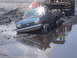 1989 Ford Bronco - A blue Ford pickup truck is stuck in a mud pit, with a large loader vehicle behind it.