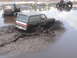 1989 Ford Bronco - A 1989 Ford Bronco navigates a muddy obstacle course, kicking up water and dirt.