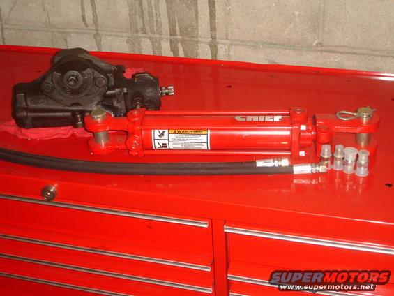 Black power steering gearbox and red hydraulic cylinder with hose and fittings on a red toolbox