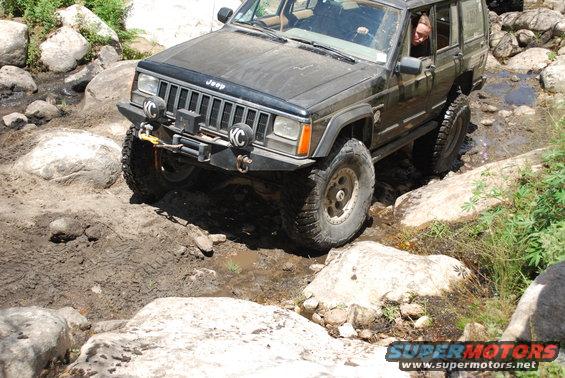 Jeep Cherokee XJ navigating a rocky, muddy trail with large boulders