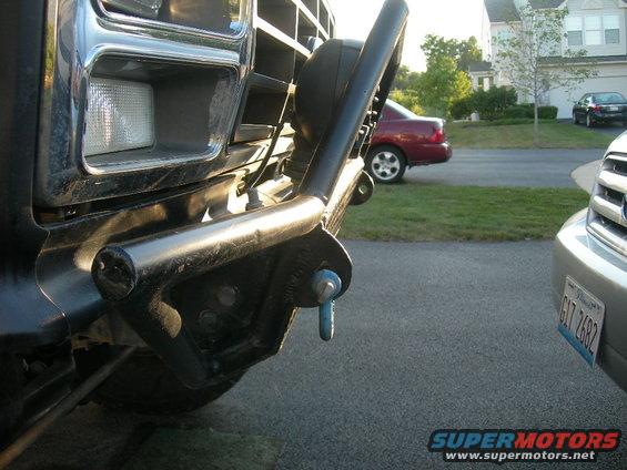 Black Ford Bronco front bumper with a tow hook and a chrome grille. A red car is visible in the background