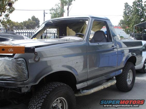 Gray Ford Bronco with a damaged windshield and missing side windows, parked outdoors