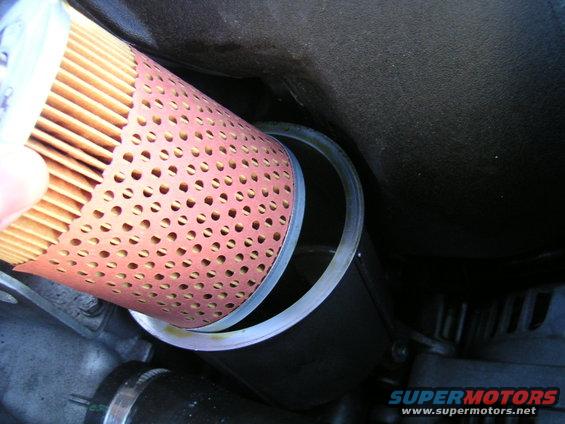 Oil filter being removed from its housing, showing perforated metal and rubber gasket