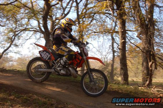 Orange dirt bike with number 461 on rear fender, ridden by a person in yellow and black gear