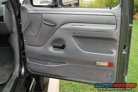 Gray interior door panel with manual window crank, power lock button, and storage compartments