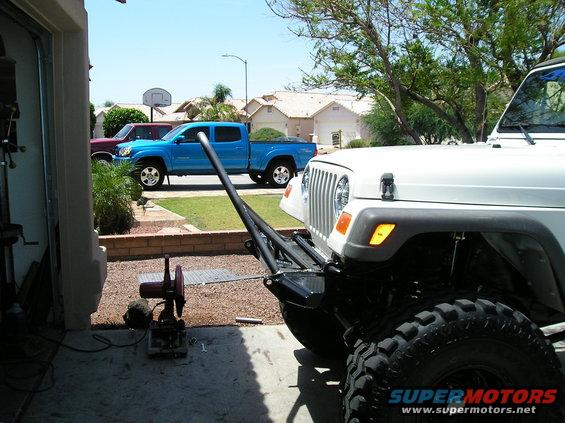 White Jeep Wrangler front end with aftermarket bumper, blue pickup truck and red truck in background