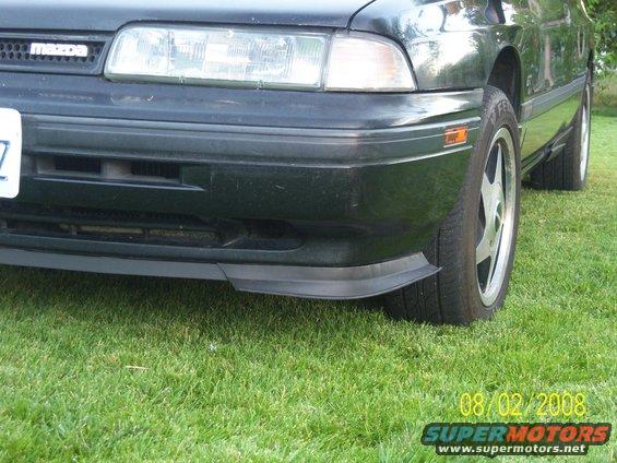 Front bumper and wheel of a dark green car with a lip spoiler