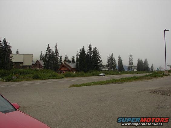 White sedan driving on a road with houses and trees in the background