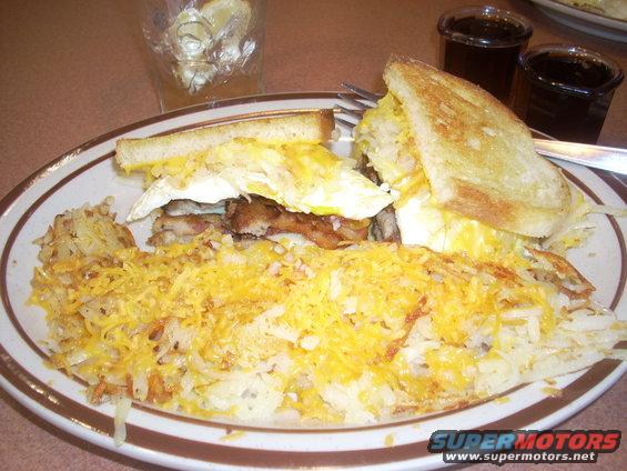 Breakfast sandwich with fried egg, cheese, and bacon served with shredded hash browns and melted cheese