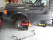 1991 Ford Bronco - The front end of a dark-colored Ford Bronco is elevated on jack stands in a garage, undergoing maintenance.