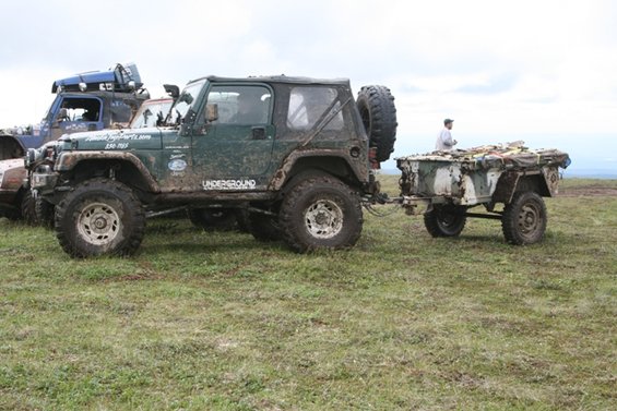 Green off-road vehicle with spare tire on back, towing a trailer in a grassy field