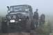 1990 Chevrolet Suburban - A modified Jeep Wrangler sits on a muddy trail, with a person standing beside it in foggy conditions.