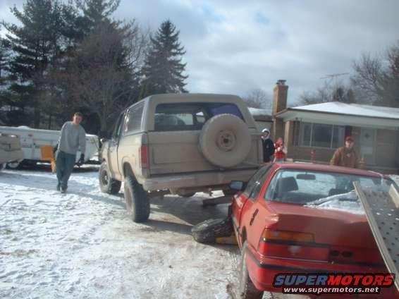 Tan Ford Bronco with a spare tire on the back, parked in snow next to a red car