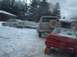 1986 Ford Bronco - A tan Ford Bronco from the 1980s is seen from the rear, parked in a snowy lot next to other vehicles.