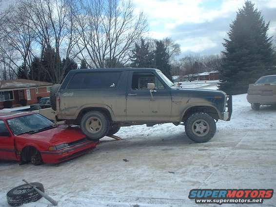 Ford Bronco parked on top of a red sedan in a snowy area