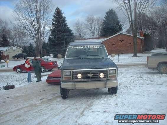 Dark blue Ford Bronco with 'Mumbly's Off Road' on windshield, parked in snowy driveway. Red car and pickup truck also visible