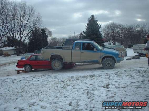 Pickup truck on top of a red car in a snowy lot
