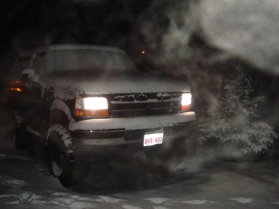 Ford truck with snow on it, headlights on, in a snowy area at night. License plate BYX-683 visible