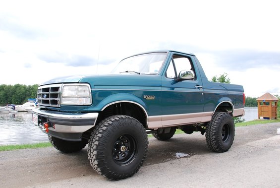 Teal 1996 Ford Bronco with beige trim and large off-road tires parked by a lake