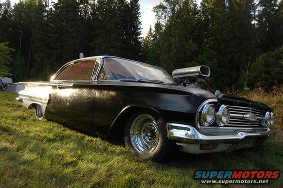 Customized black 1959 Chevrolet Impala with a large blower scoop on the hood, parked on grass