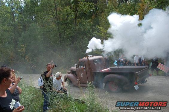 Old brown pickup truck with smoke coming from exhaust pipe, people watching